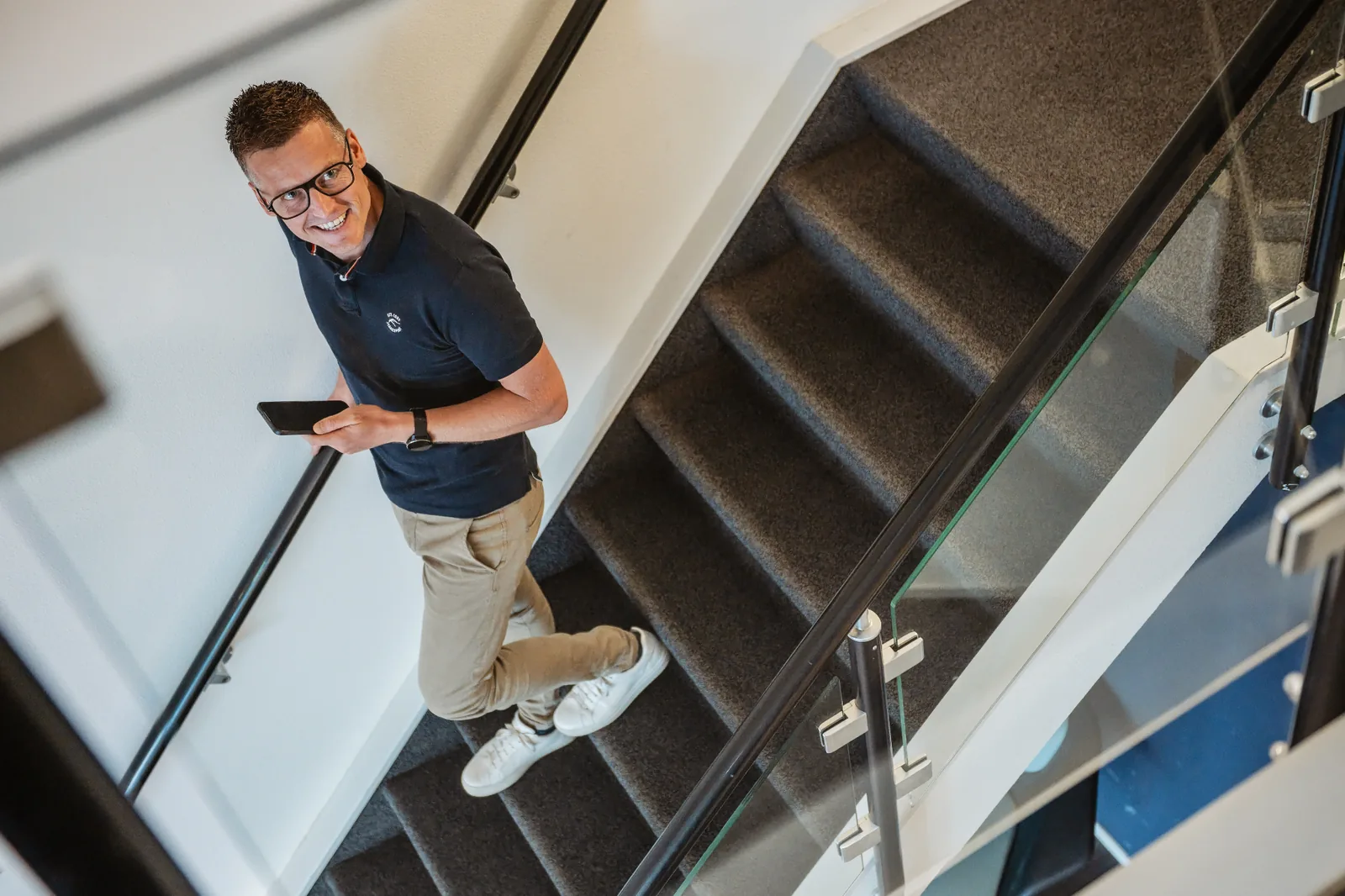 Collega van PoortEijk loopt lachend de trap op met telefoon in de hand op kantoor in Leusden